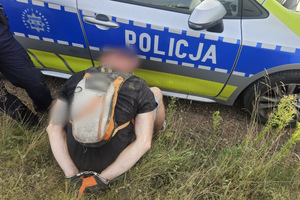 Na zdjęciu widać radiowóz, policjanta oraz zatrzymanego mężczyznę.