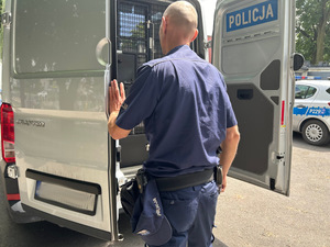 Na zdjęciu widać policjanta zamykającego drzwi radiowozu.