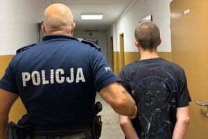 Na zdjęciu widać policjanta, który prowadzi mężczyznę w kajdankach.