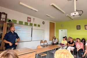 Na zdjęciu widać policjanta w sali oraz zgromadzone osoby podczas konferencji.