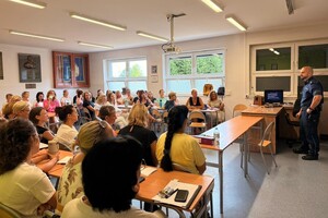 Na zdjęciu widać policjanta w sali oraz zgromadzone osoby podczas konferencji.