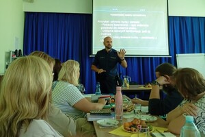Na zdjęciu widać policjanta w sali oraz zgromadzone osoby podczas konferencji.