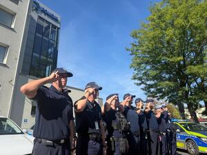 Na zdjęciu widać policjantów i policjantki żorskiej komendy Policji zgromadzonych na parkingu przed budynkiem i oddający honor poległemu koledze.