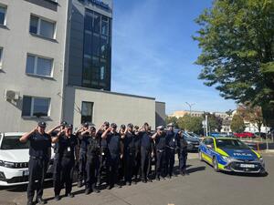 Na zdjęciu widać policjantów i policjantki żorskiej komendy Policji zgromadzonych na parkingu przed budynkiem i oddający honor poległemu koledze.