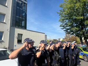 Na zdjęciu widać policjantów i policjantki żorskiej komendy Policji zgromadzonych na parkingu przed budynkiem i oddający honor poległemu koledze.