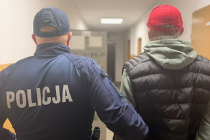 Na zdjęciu widać policjanta oraz zatrzymanego mężczyznę w czerwonej czapce.