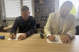 Na zdjęciu widać policjanta oraz mężczyznę siedzących przy biurku, na którym leżą dokumenty.