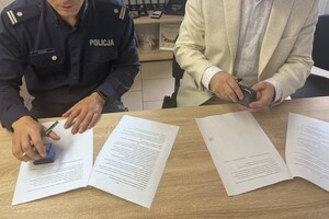 Na zdjęciu widać policjanta oraz mężczyznę siedzących przy biurku, na którym leżą dokumenty.